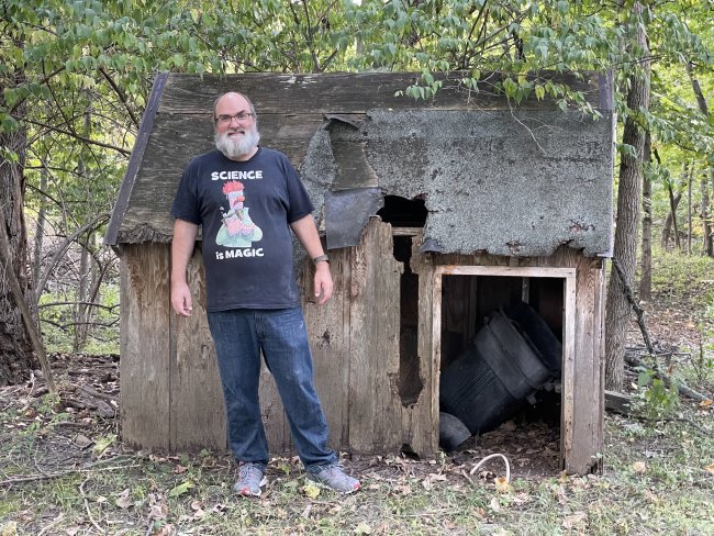 Christopher in front of a child's playhouse that has fallen to ruin. The wood is rotting, the shingles are nearly all missing and it is falling apart. We have a story about this place, but that's for another day.